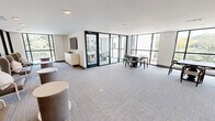 Located at 5102 Station Dr in Birmingham, Alabama, this single-floor amenity space offers a thoughtfully designed environment that blends comfort with contemporary style. The open-plan layout encompasses a combined living and dining area, bathed in abundant natural light courtesy of expansive floor-to-ceiling windows with sleek black frames that offer sweeping views of the surrounding greenery and neighborhood streetscape.

The living area is appointed with high-backed lounge chairs, cylindrical side tables, and a wall-mounted flat-screen television set atop a cream-toned credenza — creating an inviting setting for casual gatherings or relaxed socializing. Adjacent to this lounge zone, a dining area provides multiple seating arrangements with dark wood tables and mixed seating options suited for both collaborative and independent use.

A glass-walled private conference or dining room is accessible via a bold black-framed door, offering a more intimate setting centered around a long white table with upholstered chairs and anchored by a statement pendant light. This enclosed room benefits from its own set of large-pane windows, reinforcing the connection to the outdoors.

Throughout the space, neutral-toned carpet, recessed lighting, and clean white walls contribute to a bright, polished ambiance. Decorative accents — including artwork, table lamps, and a sideboard with gold hardware — add warmth and character to this well-appointed communal space.