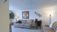 Located at 2144 Lakeshore Dr. in Ridgeland, Mississippi, this single-floor home presents a straightforward and functional layout well-suited for comfortable everyday living. The living area serves as a central gathering space, featuring soft wall-to-wall carpeting that adds warmth underfoot and a textured ceiling that lends a classic residential character to the room. The space is finished with light-toned walls that create a bright, neutral backdrop, allowing for flexible furnishing and décor choices. The living room provides ample space for seating arrangements, with room for multiple furniture pieces and accent elements. Subtle decorative touches, such as wall art and metallic accents, contribute to the home's inviting ambiance. The overall design reflects a traditional aesthetic, emphasizing comfort and practicality throughout. Situated in the Ridgeland area of Mississippi, this home benefits from its established neighborhood setting along Lakeshore Drive, offering residents a quiet and accessible residential environment. The single-floor plan ensures ease of movement throughout the home, making it a practical and welcoming space for a variety of lifestyles.