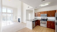 This two-story, two-bedroom, one-bathroom home offers a well-organized layout across two floors, with the main living areas on the ground floor and bedrooms located above. The main level is anchored by a bright, open living room distinguished by dramatically high ceilings, large sliding glass doors, and a clerestory window that flood the space with natural light. A fireplace with a clean white mantle adds a focal point to the living area, which features soft wall-to-wall carpeting. The kitchen is thoughtfully designed with warm cherry wood cabinetry, granite countertops, a peninsula with a sink, and a full suite of stainless steel appliances including a range, microwave, and refrigerator. Light hardwood-style flooring ties the kitchen and entry areas together. A carpeted staircase with a white railing leads to the upper floor, where both bedrooms are located. Each bedroom is carpeted and receives natural light through windows fitted with blinds. The primary bedroom includes a closet with built-in shelving. The bathroom features a granite-topped vanity with rich wood cabinetry, tile flooring, and a full soaking tub with a tiled surround. The home also includes a hallway and closet, rounding out a functional and comfortable layout.