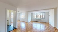 Located at 2128 Cathedral Ave NW in Washington, DC's Cathedral Heights neighborhood, this single-floor residence combines classic architectural details with functional updates throughout. The most distinctive design element found consistently across the space is the warm parquet wood flooring, laid in a traditional block pattern that adds character and visual texture to every room.

The expansive main living area is a standout feature, characterized by generous proportions and multiple large windows that flood the space with natural light and offer views of surrounding trees. A radiator unit beneath the windows provides efficient heating, while the crisp white walls create a bright, open atmosphere. The layout flows naturally from the living area toward the kitchen and private rooms.

The kitchen is well-appointed with white cabinetry, dark granite-style countertops, and a full suite of stainless steel appliances including a gas range, microwave, and dishwasher. A window above the sink brings in additional natural light.

The bedroom features two side-by-side closets providing ample storage, along with a window overlooking greenery. A secondary room with its own door offers flexibility. The bathroom is finished with classic white subway tile in the tub surround and a charming green-and-white mosaic tile floor, complemented by a modern vanity with a dark countertop.