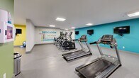 Located at 1020 Paisley Rd in Guelph, Ontario, this fitness centre offers a comprehensive, single-floor workout facility designed to support a wide range of exercise routines. The open-plan layout provides ample space for movement, with a durable speckled flooring surface underfoot and bright, recessed panel lighting overhead that ensures the entire area is well-illuminated.

The cardio zone is prominently featured, housing a row of Matrix-brand treadmills and elliptical trainers positioned alongside a teal accent wall. Wall-mounted flat-screen televisions are conveniently placed for viewing during workouts. The strength training area is anchored by a full-length mirror wall that enhances the sense of openness, and includes a dumbbell rack, weight bench, and multi-function strength machines. Stability balls and additional accessories are neatly stored nearby.

The facility is further distinguished by vibrant accent walls in teal, green, and yellow, along with a bold motivational typography mural featuring words such as "Dedication," "Commitment," and "Aim Higher." Safety is addressed through a clearly mounted AED (defibrillator) station. Decorative touches, including framed artwork and a tall ornamental plant, contribute to an energetic yet welcoming atmosphere. Overall, the space is thoughtfully organized to accommodate both cardio and strength training needs efficiently.