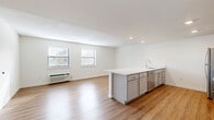 Located at 210 Senate Ave in Camp Hill, PA, this one-bedroom, one-bathroom unit offers a well-organized single-floor layout designed for comfortable everyday living. The open-concept kitchen and living area serves as the heart of the unit, featuring warm hardwood-style flooring, recessed lighting, and a peninsula with a white countertop that doubles as a breakfast bar. The kitchen is equipped with stainless steel appliances, including a refrigerator, electric range, over-the-range microwave, and dishwasher, complemented by gray shaker-style cabinetry and a subway tile backsplash. An adjacent pantry provides additional storage convenience. The living area is bright and airy, with multiple windows fitted with blinds that allow natural light to fill the space. The bedroom offers a carpeted floor, a wall-unit HVAC system, a window with outdoor views, and two generous closets. A hallway connects the living spaces to the full bathroom, which includes a tub/shower combination, a vanity with gray cabinetry, and matching hardwood-style flooring. A utility room and additional closet round out the practical amenities of this neatly appointed unit.