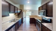 This single-floor residence is thoughtfully designed with a cohesive aesthetic defined by rich dark wood cabinetry, hardwood-style flooring, and neutral wall tones throughout. The galley-style kitchen is a functional centerpiece, featuring stainless steel appliances including a refrigerator, electric range, and built-in microwave, complemented by granite-look countertops and a double-basin sink. Upper and lower dark cabinetry provides ample storage, while a peninsula connects the kitchen to the dining area, which is illuminated by a decorative chandelier and benefits from natural light and balcony access through a sliding glass door.

The open living area is spacious, finished with hardwood-style flooring, a ceiling fan, and baseboard heating. Multiple windows invite natural light and outdoor views. Bedrooms are carpeted for comfort, each offering closet access — one featuring a walk-in closet with built-in shelving — and baseboard heating.

The bathrooms are consistently styled with dark vanity cabinetry, white countertops, and hardwood-style flooring. A full bathroom connects directly to the primary bedroom, while an additional bathroom serves the remaining rooms. Hallways are well-lit and efficiently laid out, tying the unit's spaces together seamlessly.