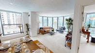 Located along East South Water Street in Chicago's vibrant Streeterville neighborhood, this single-floor residence offers a well-organized layout filled with natural light and impressive urban views. The living area is a standout feature, anchored by expansive floor-to-ceiling windows that frame sweeping Chicago skyline panoramas, flooding the space with daylight. Plush carpeting runs throughout the living and sleeping areas, contributing to a comfortable, cohesive feel. A distinct accent wall in a soft blue-grey tone adds visual interest to the secondary living area, which connects seamlessly to the dining space.

The galley-style kitchen features warm wood cabinetry, tile flooring, and full appliances, offering an efficient and practical cooking environment. The bedrooms are generously proportioned, with the primary bedroom benefiting from large sliding glass windows that overlook green outdoor space and the surrounding cityscape, along with a walk-in closet for ample storage.

Two bathrooms mirror each other in design, each featuring a tub-shower combination with tile surrounds, warm wood vanities, and wide mirrors with integrated lighting. The overall ambiance throughout is clean, bright, and contemporary, suited to the dynamic urban environment of downtown Chicago.