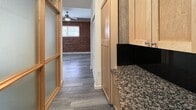 Located at 402 North 18th Street in Richmond, Virginia, this efficiently designed unit offers a thoughtful layout across a single floor. The space is characterized by durable grey hardwood-style flooring that runs throughout, creating a cohesive and modern aesthetic.

A standout architectural detail is the use of frosted glass partition doors with warm wood frames, which divide the living areas while allowing diffused light to pass between spaces. These panels lend the unit a contemporary, loft-inspired character. The living area features an exposed red brick accent wall, adding historic charm and texture, complemented by a ceiling fan that enhances airflow and comfort.

The kitchen is well-appointed with light maple cabinetry, dark granite countertops with a black tile backsplash, and stainless steel appliances, including a range and dishwasher. A dedicated bedroom area offers clean white walls and ample room, with neutral tones that provide a versatile backdrop. The bathroom is finished with tile flooring, a vanity with wood cabinetry, and standard fixtures.

A central hallway connects the kitchen, bedroom, and bathroom, facilitating an efficient flow through the unit. The combination of exposed brick, frosted glass partitions, and granite finishes gives this space a distinctive character that balances modern updates with classic Richmond architectural elements.
