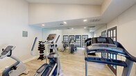 This fitness center at 7670 N Oakbrook Dr in Reynoldsburg, Ohio, offers a well-appointed exercise space designed to maximize both functionality and comfort. The room features light hardwood-style flooring throughout, which pairs cleanly with bright white walls and a neutral color palette to create an open, energizing atmosphere. Recessed lighting provides consistent illumination across the space, complemented by a window that allows natural light to filter in and offers a view of the outdoor surroundings.

A full wall of floor-to-ceiling mirrors visually expands the room while allowing users to monitor their form during workouts. The fitness center is equipped with a range of cardio machines, including NordicTrack treadmills, an elliptical trainer, and a stationary recumbent bike. A vertical dumbbell rack with multiple weight options rounds out the strength training offerings. Stylish black-framed French doors serve as the room's entry point, adding an elegant architectural detail that sets this space apart from a typical gym aesthetic. The elevated ceiling height on one side of the room further contributes to the sense of openness. Altogether, this fitness center delivers a clean, modern, and fully functional workout environment.