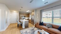 This thoughtfully designed 1-bedroom, 1-bathroom residence spans a single floor and maximizes every square foot with a smart, open-concept layout. The kitchen is a standout feature, showcasing warm wood-toned cabinetry, a full suite of stainless steel appliances including a French door refrigerator, electric range, microwave, and dishwasher, and a generous island with a white quartz countertop that doubles as a breakfast bar with seating. Stylish pendant lighting illuminates the space, which flows seamlessly into the living room. The living area benefits from large windows dressed with blinds and floor-length curtains, filling the space with natural light and offering outdoor views. Light wood-style flooring extends throughout the main living areas, adding warmth and continuity. The bedroom is a comfortable retreat featuring plush carpeting, a ceiling fan, and a window with outdoor views. A dedicated closet provides organized storage. The bathroom is clean and functional, featuring a wood-toned vanity with a white countertop, an undermount sink, and a full tub-shower combination. The overall ambiance is modern and inviting, characterized by a neutral color palette, contemporary finishes, and a cohesive design that balances style with practicality.