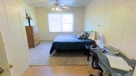 This unit at The Metropolitan Apartments offers a practical and comfortable living space spread across a single floor. The bedroom is a highlight of the space, featuring a large window that invites ample natural light, creating a bright and welcoming atmosphere. A ceiling fan with integrated lighting is centrally positioned, ensuring year-round comfort and efficient air circulation. The room accommodates a full-sized bed with generous floor space remaining, and the combination of hardwood flooring near the entry and a plush area rug adds both warmth and texture to the environment. A dedicated desk area provides a functional workspace, making the room versatile for both rest and productivity. Additional storage is offered by a classic wooden dresser, contributing to the room's practical layout. The neutral wall tones throughout keep the space feeling open and adaptable to a variety of personal styles. Overall, this unit offers a well-balanced blend of comfort, functionality, and natural light, making it a suitable residence for those seeking a straightforward and livable space at The Metropolitan Apartments.