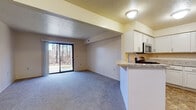 Located at 22644 Pine Arbor Dr in Elkhart, Indiana, this single-floor unit offers a straightforward, functional layout designed for comfortable everyday living. The open-concept living and kitchen area forms the heart of the space, where soft carpeting extends throughout the living zone while tile flooring grounds the kitchen. A sliding glass door at the far end of the living area fills the room with natural light and provides views of surrounding trees, creating a connection to the outdoors.

The kitchen is well-appointed with crisp white shaker-style cabinetry, light granite-look countertops, and stainless steel appliances including a gas range and over-the-range microwave. A peninsula with an integrated sink and breakfast bar seating separates the kitchen from the living area, offering both additional prep space and a casual dining option. A refrigerator and dishwasher complete the appliance package.

A dedicated bedroom features plush carpeting, a window with exterior views, and a louvered bifold closet door providing ample storage. The full bathroom is finished with tile flooring and includes a standard tub-shower combination. The overall palette of neutral tones throughout the unit creates a clean, move-in-ready atmosphere.