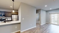 Located at 5510 Southwestern Blvd in Hamburg, NY, this well-appointed 2-bedroom, 2-bathroom single-floor unit offers a thoughtfully designed layout with modern finishes throughout. The open-concept kitchen is a standout feature, outfitted with dark shaker-style cabinetry, stainless steel appliances including a gas range, microwave, and refrigerator, white quartz countertops, a peninsula with an undermount sink, and pendant lighting that adds a contemporary touch. The kitchen flows naturally into the living area, which is bright and airy with recessed lighting, light-toned hardwood-style flooring, and sliding glass doors that lead to a balcony with views of the surrounding community. The two bedrooms are carpeted for comfort, each with windows allowing natural light. The primary bedroom is generously sized and connects to a full bathroom featuring a glass-enclosed shower and access to a walk-in closet with built-in wire shelving. The second bathroom is equally well-finished, with a dark navy vanity, white quartz countertop, and wood-look flooring. A dedicated hallway and closet provide additional organization and storage. Neutral gray walls, white trim, and black hardware accents lend a cohesive, modern aesthetic throughout the entire space.