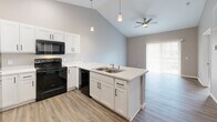 Located at 3276 Jim St in Rapid City, South Dakota, this well-designed one-bedroom, one-bathroom unit offers a thoughtful layout that maximizes every square foot of its compact footprint. The open-concept living and kitchen area immediately draws attention with its striking vaulted ceiling, which lends a spacious, airy quality to the main living space. Light gray walls and durable wood-look luxury vinyl plank flooring run throughout the common areas, creating a clean, contemporary aesthetic.

The kitchen is a standout feature, anchored by a peninsula with a double-basin stainless steel sink, crisp white shaker cabinetry, and light quartz-style countertops. Black appliances — including a range, microwave, dishwasher, and refrigerator — add a modern contrast. Pendant lighting above the peninsula and recessed ceiling lights provide both task and ambient illumination. The open layout connects the kitchen seamlessly to the living area, which is finished with a ceiling fan and access to natural light through large sliding doors.

The bedroom is a comfortable, carpeted retreat featuring neutral gray walls, a bright window with neighborhood views, and direct access to a dedicated closet with a full rod and shelf system. A practical in-unit laundry area with a full-size washer and dryer adds significant everyday convenience. The bathroom and closet round out this efficient, move-in-ready home.