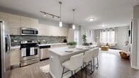 Located at 100 Aqua Way in Newport, Kentucky, this well-appointed 2-bedroom, 2-bathroom residence offers a thoughtfully designed single-level layout with modern finishes throughout. The open-concept kitchen serves as the heart of the home, featuring light wood cabinetry, a decorative tile backsplash, stainless steel appliances, and a central island with seating — ideal for both cooking and casual dining. Pendant lighting and track fixtures add a contemporary touch overhead, while wood-look flooring grounds the space with warmth. The living room is generously proportioned, filled with natural light from large windows with floor-length drapes, and opens to a balcony. Neutral gray tones and clean lines create a calming, cohesive atmosphere. Both bedrooms offer plush carpeting and ceiling fans, with the primary bedroom featuring an en-suite bathroom and walk-in closet with built-in shelving. The primary bath includes a sleek floating vanity with a white quartz countertop and a glass-enclosed shower. The second bathroom mirrors the modern aesthetic with a soaking tub, tiled surround, and matching vanity. Two closets provide ample storage throughout the residence.