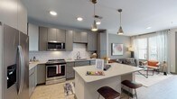 Located at 1005 W Main St in Durham, NC, this single-floor residence offers a thoughtfully designed open-concept layout with contemporary finishes throughout. The kitchen is a standout feature, showcasing flat-front gray cabinetry, white quartz countertops, a classic subway tile backsplash, and a full suite of stainless steel appliances. A central island with seating provides both additional prep space and a casual dining area, while pendant lighting adds an industrial-modern touch. Light wood-style flooring runs throughout, creating a warm, cohesive aesthetic. The living area flows naturally from the kitchen, offering a comfortable and well-lit space accented by soft neutral tones and curated artwork. The bedroom is highlighted by a bold navy accent wall, ceiling fan, and generous natural light from large windows dressed with layered curtains and blinds. The bathroom is equally refined, featuring gray cabinetry, a wide vanity mirror, quartz countertops, and a glass-enclosed walk-in shower clad in oversized white subway tile. An in-unit washer and dryer adds everyday convenience. The overall ambiance is modern and polished, blending clean architectural lines with warm, livable design elements suited for contemporary urban living.