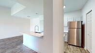 Located at 22743 Preakness Blvd in Land O' Lakes, Florida, this single-floor residence offers a clean, modern aesthetic with a well-designed open layout. The living area is a standout feature, boasting vaulted ceilings that enhance the sense of space and airiness. Wood-look plank flooring runs throughout the main living areas, providing a warm and cohesive feel. A ceiling fan adds comfort, while sliding glass doors open to a private balcony, filling the room with natural light and offering pleasant outdoor views.

The kitchen is thoughtfully designed with white shaker-style cabinetry, white countertops, and a full suite of stainless steel appliances, including a refrigerator, electric range, and over-the-range microwave. A peninsula with a deep undermount sink and a modern pull-down faucet provides additional prep and casual dining space, seamlessly connecting the kitchen to the living area.

The bedrooms are carpeted for comfort, with vaulted or elevated ceilings adding dimension. At least one bedroom features a walk-in closet and access to natural light through a window. The bathroom is finished with wood-look tile flooring, white cabinetry, and a tiled shower, maintaining the home's consistent, neutral design palette throughout.