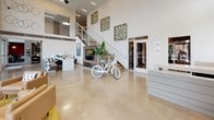 Located at 530 11th Ave N in Nashville's vibrant Gulch neighborhood, this contemporary single-floor commercial lobby combines industrial design with modern sophistication. Polished concrete floors extend throughout the entire space, complementing the soaring double-height ceilings that flood the interior with natural light through expansive floor-to-ceiling glass windows and doors. The entry vestibule welcomes visitors with bold abstract artwork, concrete columns, and direct views of the surrounding urban streetscape. A central open-plan lounge area is furnished with warm tan leather seating arrangements set atop golden-yellow area rugs, creating an inviting gathering space bathed in natural light from the oversized windows overlooking 11th Avenue. A striking wood-and-glass barn-style sliding door divides the main floor, adding an architectural focal point alongside a walnut-topped bar counter with seating — ideal for casual meetings or collaborative work. An upper mezzanine level with glass railings overlooks the main floor, enhancing the sense of vertical space. A dedicated coffee bar, outfitted with a Lavazza machine, dark wood cabinetry, and wall-mounted organizer racks, provides a functional refreshment nook. Curated artwork and decorative accents throughout contribute to a polished yet approachable ambiance.