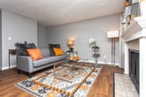 This single-floor residence offers a well-organized layout designed for comfortable everyday living. Neutral gray walls and warm hardwood-style flooring run consistently throughout the space, creating a cohesive and inviting atmosphere.

The living area connects to a hallway leading to the private quarters, with a console table and decorative accents contributing to a modern, styled aesthetic. A dedicated dining area adjoins the kitchen and benefits from a sliding glass door dressed with vertical blinds, allowing natural light to filter in. A pendant chandelier overhead adds a subtle focal point to the dining space.

The kitchen features rich, dark wood cabinetry extending to the upper walls, light-toned countertops, a stainless steel sink, and black appliances, offering ample storage and functional prep space in an efficient L-shaped configuration.

Two bedrooms provide comfortable retreats, each finished with the same warm flooring and soft neutral walls. A textured ceiling adds architectural detail throughout. Both bathrooms are cleanly appointed with white vanities, single-sink countertops, large mirrors, and shower-tub combinations enclosed by curtains, offering practical and tidy facilities. The overall ambiance of the space is understated and move-in ready.