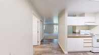 Located in Everett, WA, this studio offers a practical and comfortable single-floor layout. The entry transitions seamlessly from wood-style LVP flooring into the open living area, which is finished with plush carpeting and bathed in natural light from a sliding glass door. The door opens to a private balcony with metal railing, offering tranquil views of surrounding evergreen trees. A ceiling fan provides added comfort to the living space.

The galley-style kitchen is efficiently designed with white cabinetry extending to the ceiling, granite-look countertops, and white appliances including a range and full-sized refrigerator. A built-in dishwasher and stainless steel sink complete the functional workspace, while a skylight brightens the room.

The full bathroom features wood-style flooring consistent with the entryway, a tub/shower combo with a curved curtain rod, a toilet, and a vanity with granite-look countertop and mirrored medicine cabinet. A closet is conveniently accessible from the main hallway, providing useful storage.

Throughout, the unit maintains a clean, neutral color palette with white walls and trim, creating a bright and welcoming atmosphere that makes efficient use of its compact footprint.