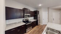 Located in Fort Mill, SC, this single-floor home offers a well-designed layout with thoughtful finishes throughout. The kitchen is a standout feature, boasting rich dark espresso cabinetry, granite-look countertops, a classic white subway tile backsplash, and a full suite of stainless steel appliances including a range, microwave, and refrigerator. A peninsula with an integrated sink adds both functionality and additional workspace. Wood-look plank flooring runs through the main living and kitchen areas, lending warmth and continuity to the open layout. The living area is bright and open, with natural light filtering through large windows. Bedrooms are carpeted and feature ceiling fans with light fixtures and windows overlooking greenery outside. A generously sized walk-in closet with wire shelving and basket storage provides ample organization space. The primary bathroom is well-appointed with dark cabinetry, a wide vanity with a large mirror, a three-bulb vanity light fixture, and a separate glass-enclosed shower. A secondary bathroom offers a full tub-shower combo, dark vanity, and tile flooring. Completing the home is a dedicated laundry room with a full-size top-loading washer and dryer and overhead wire shelving for added storage.
