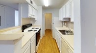 This single-floor residence offers a well-organized layout designed for comfortable everyday living. The galley-style kitchen is efficiently arranged with white cabinetry lining both sides, light countertops, a stainless steel sink, an electric range, and a full-size refrigerator. Hardwood-style flooring runs throughout the kitchen, adding warmth to the space. A textured ceiling and bright overhead lighting keep the area feeling clean and functional.

The living area is generously sized, featuring neutral carpet, white walls, and a textured ceiling. A full-width sliding glass door with vertical blinds opens to an outdoor patio, allowing natural light to flow in. Adjacent to the living space is a carpeted entry area with a front door and a recessed ceiling light.

The bedrooms are carpeted and bright, each with windows that bring in natural light. The primary bedroom includes direct access to a private bathroom and an additional doorway, likely leading to a closet or hallway. The secondary bedroom features a ceiling-mounted light fixture.

The bathroom is equipped with a wide vanity topped with a light countertop, white cabinetry below, a large wall mirror, and a Hollywood-style light bar above. A dedicated laundry area houses a full-size GE washer and dryer side by side, with a storage shelf mounted above for added convenience.