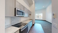 This efficiently designed single-floor unit offers a thoughtful layout across five distinct spaces, making excellent use of every square foot. The entrance welcomes you into a hardwood-style flooring corridor that transitions seamlessly into the main living areas.

The galley-style kitchen is a standout feature, outfitted with sleek gray cabinetry, marble-look countertops, and a full suite of stainless steel appliances including an electric range, dishwasher, over-the-range microwave, and refrigerator. A tile backsplash adds a refined touch, and recessed lighting keeps the space bright and functional. Notably, an in-unit stacked washer and dryer is conveniently tucked adjacent to the kitchen area, along with an electrical panel access point.

The living room impresses with dramatically high ceilings that lend an open, airy feel to the space. Plush gray carpeting, crisp white walls, and a large window allow natural light to pour in, offering views of the surrounding greenery. A wall-mounted mini-split unit provides climate control, and a lean-to ladder hints at potential loft storage above.

The bathroom is clean and functional, featuring wood-look flooring, a vanity with a marble-look countertop, and a chrome towel bar. A dedicated closet provides essential storage, completing this well-organized and modern unit.