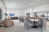 This single-story community clubhouse in Idaho Falls, Idaho offers a generously sized, thoughtfully designed gathering space that blends modern aesthetics with welcoming functionality. The main lounge area is anchored by soaring ceilings and expansive black-framed windows that flood the interior with natural light and frame views of the surrounding outdoor amenities, including a pool area. Crisp white walls, light-toned carpeting, and wood-accented flooring create a clean, contemporary backdrop throughout.

The lounge is furnished with an inviting mix of neutral and bold orange upholstered seating arranged across multiple social zones, complemented by a linear fireplace, sculptural wall art, and elegant pendant lighting. A dining nook features built-in banquette seating with warm wood tables and swivel chairs beneath clerestory windows, ideal for casual gatherings.

An adjacent game room makes a bold architectural statement with a striking red coffered ceiling and globe pendant lights. This lively space accommodates arcade machines and a ping-pong table, offering a vibrant contrast to the lounge's refined atmosphere.

Additional seating areas incorporate marble-top accent tables and carefully curated greenery, enhancing the overall sense of warmth and sophistication. Together, these spaces form a dynamic, well-appointed clubhouse designed for both relaxation and socializing.