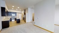 This 1-bedroom, 1-bathroom residence is designed with an open-concept layout that seamlessly connects the living area to the kitchen, creating a spacious and functional flow throughout. The kitchen is a standout feature, equipped with stainless steel appliances including a refrigerator and range, dark cabinetry that contrasts beautifully against light walls, and a central island that provides additional prep space and storage. Recessed lighting illuminates the kitchen area, adding a clean, modern touch to the ceiling. The living area is finished with light-toned flooring that extends throughout, lending a warm and cohesive feel to the space. Neutral, light-colored walls contribute to a bright and airy ambiance, while the open sightlines between rooms enhance the sense of space. A hallway leads to the bedroom and bathroom, offering a natural separation between the living and private areas of the home. The unit is a single-floor layout, making it highly accessible and easy to navigate. Overall, the space strikes a balance between contemporary design and everyday practicality, making it a comfortable and inviting place to call home.