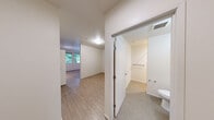 Located at 4303 7th Ave NE in Seattle's University District, this single-floor unit offers an efficient, well-organized layout across a compact footprint. The space is designed to maximize functionality while maintaining a clean, modern aesthetic throughout.

The kitchen serves as a focal point of the unit, featuring warm-toned wood cabinetry that extends to the ceiling, providing ample storage. It is fully equipped with stainless steel appliances, including a gas range, built-in microwave, dishwasher, and refrigerator. Light-colored countertops complement the cabinetry, and a pendant track lighting fixture overhead adds a contemporary touch. A window positioned beside the kitchen offers natural light and a view of the surrounding streetscape.

The open living area flows directly from the kitchen, finished with light wood-style hard flooring that runs throughout the main living space. The room features neutral white walls, a ceiling-mounted smoke detector, and floor-level HVAC vents, keeping the design clean and unobtrusive.

The bathroom includes carpeted flooring and a grab bar, offering practical accessibility features. A dedicated entrance area with additional carpeting and built-in hanging hardware provides a functional transition into the unit. Overall, the space presents a straightforward, move-in-ready design well-suited to urban living.