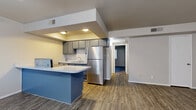 Located in Cave Creek, AZ, this single-floor residence offers three bedrooms and one bathroom within a thoughtfully laid-out floor plan. Wood-look plank flooring runs consistently throughout the home, lending a cohesive and modern aesthetic to every room.

The kitchen serves as a functional centerpiece, featuring gray cabinetry, a white countertop peninsula with a bold blue base, stainless steel refrigerator, and a dedicated sink area. A recessed soffit with built-in lighting frames the kitchen, creating a defined and well-lit cooking space that opens toward the living area.

The living room is bright and open, benefiting from multiple windows dressed with vertical blinds that allow ample natural light to filter in. The front entry, flanked by two windows, contributes to the airy feel of the common area.

Each of the three bedrooms is modestly sized with neutral wall tones and wood-look flooring. The bedrooms include sliding-door closets with built-in rods for storage. The primary bedroom offers a comfortable layout with its own closet access.

The bathroom is clean and functional, equipped with a full tub-shower combination, toilet, and a vanity with gray cabinetry. The consistent flooring carries into this space as well, maintaining visual continuity throughout the home.