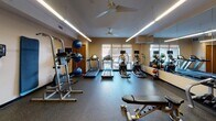 Located at 2915 Knox Ave S in Minneapolis, Minnesota, this fitness center offers a comprehensive, single-floor workout facility designed to support a wide range of exercise routines. The space is thoughtfully laid out to maximize functionality and flow, with durable rubber flooring throughout that provides both safety and comfort during workouts.

The cardio zone is well-equipped with multiple treadmills and elliptical machines positioned near large windows, allowing natural light to fill the space and providing a connection to the outdoors during exercise. Ceiling fans overhead contribute to a comfortable workout environment, complemented by sleek linear LED lighting that ensures consistent, bright illumination throughout.

A dedicated strength training area features a dumbbell rack with a full range of free weights, an adjustable weight bench, a power tower for bodyweight exercises, and a Matrix stationary bike. TRX suspension training straps are mounted to the wall, adding versatility to the strength training options available.

Floor-to-ceiling mirrors line one wall, visually expanding the space and allowing users to monitor their form. Stability balls and medicine balls are neatly organized on racks, rounding out the functional fitness offerings. Built-in wooden shelving units provide additional storage and contribute warmth to the otherwise utilitarian aesthetic. The overall ambiance is clean, organized, and purpose-driven, making this fitness center a practical and well-appointed facility.
