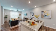 This well-designed single-story residence features an open-concept layout that seamlessly connects the kitchen, dining, and living areas. The kitchen is a standout space, equipped with stainless steel appliances, light wood-toned cabinetry, subway tile backsplash, and a granite-topped island with bar seating — ideal for both meal preparation and casual dining. Recessed lighting and wood-style flooring run throughout, lending the space a cohesive, contemporary feel.

The living room benefits from large windows dressed with sheer curtains and blinds, allowing generous natural light to fill the room. A ceiling fan overhead and a wall-mounted television add everyday comfort and functionality.

Two bedrooms each feature ceiling fans, large windows, and warm wood-style flooring. The primary bedroom offers an en-suite bathroom complete with a granite vanity, a glass-enclosed subway tile shower, and direct access to a walk-in closet. The secondary bathroom includes a full tub-shower combination and additional overhead cabinetry for storage.

A dedicated entry hallway connects all areas efficiently, reinforcing the unit's thoughtful, functional floor plan throughout.