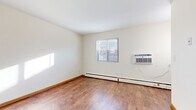 This single-floor unit offers a clean, practical layout designed for comfortable everyday living. The main living area is defined by warm hardwood flooring that flows throughout, crisp white walls, and natural light streaming in through a window fitted with horizontal blinds. A wall-mounted air conditioning unit and baseboard heating ensure year-round climate control. The space opens into a well-appointed kitchen featuring white cabinetry, a double stainless steel sink, laminate countertops, and ample upper and lower cabinet storage. The bedroom is generously proportioned, bathed in natural light from a side window, and includes a sliding-door closet with built-in shelving, offering practical storage solutions. The bathroom presents a classic aesthetic with full white square tile walls, a mosaic tile floor, a wall-mounted pedestal sink, a mirrored medicine cabinet, and a full-sized bathtub with an overhead shower. Throughout the unit, the consistent use of warm wood flooring, neutral wall tones, and clean finishes creates a cohesive and inviting atmosphere suited to a variety of lifestyles.