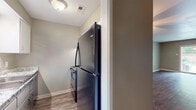 Located at 7111 Indiana Ave in Little Rock, Arkansas, this single-floor home offers a practical and comfortable layout designed for everyday living. The open living area is anchored by rich, dark hardwood-style flooring and features a ceiling fan overhead, with large sliding glass doors that invite natural light and provide direct views of the backyard. An adjacent common area continues the hardwood-style flooring and includes a pass-through window, adding a connected, open feel to the layout. The galley-style kitchen is equipped with white cabinetry, granite-look countertops, a stainless steel sink, and black appliances including a full-size refrigerator. The bedrooms are carpeted for comfort, each featuring ceiling fans and closet access, with neutral gray walls throughout. The primary bedroom includes a private en-suite bathroom with a walk-in shower, while a second full bathroom offers a tub-shower combination with chrome fixtures and wood-look flooring. Ceiling fans are present in all main living spaces and bedrooms, ensuring year-round comfort. The consistent neutral color palette and clean finishes create a cohesive, move-in-ready atmosphere throughout the home.