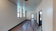 Located at 1905 Elmore St in Cincinnati, Ohio, this single-floor unit offers a clean, contemporary design throughout. The main living area is bright and open, featuring dark hardwood-style plank flooring, crisp white walls, and tall ceilings that enhance the sense of spaciousness. Large windows with horizontal blinds allow generous natural light to fill the room, creating an airy and welcoming atmosphere.

The kitchen is efficiently laid out and well-appointed with bold teal cabinetry, light-toned countertops, and a black electric range with overhead ventilation. Ample upper and lower cabinet storage makes the space highly functional for everyday use.

The bedroom area features lighter hardwood-style flooring, additional ceiling lighting, and an open closet with a hanging rod, providing convenient storage. A black refrigerator is visible nearby, seamlessly integrated into the living arrangement. An electrical panel is also accessible within this area.

The bathroom is designed with accessibility in mind, featuring stainless steel grab bars positioned near the toilet and bathtub, a teal vanity with a white countertop, and wood-look tile flooring. The dark-toned door frames throughout the unit add a modern contrast against the neutral white walls, tying the overall aesthetic together cohesively.
