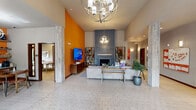 This expansive single-floor amenity center at Promenade in Auburn, WA offers a comprehensive range of facilities across a generously sized footprint. The welcoming lobby sets an immediate tone with its striking geometric tile flooring, soaring ceilings, globe pendant chandeliers, and a dramatic floor-to-ceiling blue brick fireplace flanked by eclectic shelving and a bold orange accent wall. A comfortable lounge area invites residents to relax with seating, a large-screen TV, and abundant natural light. The adjacent lounge nook continues the vibrant orange palette, featuring a kitchenette with gray cabinetry, a beverage cooler, and casual dining tables beneath stylish pendant lights. Multiple offices provide bright, functional workspaces, each featuring expansive windows with outdoor views, roller shades, and clean modern furnishings. A dedicated media room offers a wall-mounted TV, skylight, and relaxed seating. The conference room is equipped with a large wall-mounted display and modular seating for collaborative meetings. The fitness center is well-appointed with treadmills, stationary bikes, resistance equipment, and large windows that flood the space with natural light. The crown jewel is the full indoor basketball court, boasting a polished hardwood floor, soaring high windows, and branded wall padding — a standout feature that elevates the entire facility.
