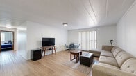 Located at 138 S Atherton St in State College, PA, this single-floor residence offers three bedrooms, two full bathrooms, and a practical, functional layout. The open living and dining area is the heart of the home, featuring light wood-look flooring, neutral white walls, and a large sliding glass door with vertical blinds that allows natural light to fill the space. The combined living and dining area provides ample room for both relaxing and entertaining. The galley-style kitchen runs along a narrow corridor and is equipped with rich dark wood cabinetry, white appliances including a refrigerator, stove, and dishwasher, along with a double sink and tile flooring. The three bedrooms are carpeted in deep blue tones and each feature windows with vertical blinds. The primary bedroom offers a comfortable footprint, while the additional bedrooms are well-suited for use as sleeping quarters or a home office. Four closets throughout the unit provide generous storage. Both bathrooms are finished with white tile walls, mosaic tile flooring, dark wood vanities, and a glass-door tub and shower combo. The unit also benefits from four closets distributed throughout for added convenience.
