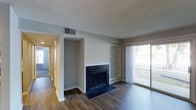 This single-floor residence offers a functional and comfortable layout designed for everyday living. The main living area serves as the heart of the home, anchored by a classic fireplace with a dark tile surround that adds a focal point to the space. Flanking the fireplace are built-in open shelves, providing practical display and storage options. Rich hardwood-style flooring extends throughout, adding warmth and visual continuity to the interior. A sliding glass door fills the living area with natural light and offers views of the outdoor surroundings, creating a bright and open atmosphere. The textured ceiling adds a traditional touch to the overall aesthetic. A hallway visible from the living area connects to additional rooms, suggesting a well-organized floor plan with clear separation between living and private spaces. The neutral gray and white color palette throughout the walls and trim creates a clean, versatile backdrop that is easy to personalize. Overall, this residence combines practical features with comfortable design elements, making it a welcoming and move-in ready space.