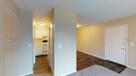 Located at 601 Wenger Rd. in Englewood, Ohio, this single-floor residence offers a practical and well-organized layout designed for comfortable everyday living. The kitchen is efficiently arranged in an L-shaped configuration, outfitted with white cabinetry, ample counter space, a built-in range with coil burners, an under-cabinet range hood, and a single-basin sink — providing all the essentials in a clean, bright setting with durable wood-style flooring underfoot. Adjacent to the kitchen, the main living area transitions between wood-style flooring and plush carpet, creating defined zones within an open feel. A dedicated entry door anchors one end of the living space. A generously sized carpeted room features a full-width sliding glass door fitted with vertical blinds, allowing natural light to fill the space and providing access to the outdoors. The bedrooms are carpeted for comfort — one includes a window for natural light, while another offers dual closets with sliding doors, providing substantial storage. The full bathroom is equipped with a soaking tub and shower combination, a toilet, and a mirrored vanity area, finished in neutral tones throughout. Warm beige walls and clean white trim carry consistently through each room, contributing to a cohesive and move-in-ready atmosphere.