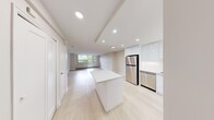 This well-designed 1-bedroom, 1-bathroom unit offers a clean, modern aesthetic throughout its single-floor layout. Light hardwood flooring runs continuously across the open-concept living and kitchen areas, enhancing the sense of space and cohesion.

The kitchen is a standout feature, outfitted with high-gloss white cabinetry extending to the ceiling, a full suite of stainless steel appliances including a refrigerator, electric range, built-in microwave, and dishwasher, and a white waterfall-edge island that doubles as a breakfast bar. Recessed lighting illuminates the space efficiently.

The living room is bright and airy, benefiting from large floor-to-ceiling windows and a glass-panel door that opens directly to an outdoor balcony, offering views of surrounding greenery. Baseboard heating runs along the window walls, ensuring year-round comfort.

The bedroom is a comfortable, well-proportioned space with a sliding glass window, baseboard heating, and light-toned walls. A dedicated closet and an in-unit stacked washer and dryer provide practical storage and laundry convenience.

The bathroom features a clean white tile surround with a soaking tub and shower combination. Throughout the unit, the consistent use of white tones, natural light, and modern finishes creates a calm, contemporary atmosphere.