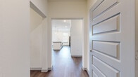 This single-floor residence is designed with a clean, contemporary aesthetic that emphasizes open living and functional comfort throughout. The heart of the home is an open-concept kitchen, which features a central island topped with granite countertops and illuminated by stylish pendant lighting. Shaker-style cabinetry in a soft gray or white finish pairs with a classic subway tile backsplash, while stainless steel appliances—including a refrigerator, range, and microwave—complete the well-equipped space. Rich hardwood-style flooring flows through the main living areas, adding warmth and continuity.

The living area is bright and airy, benefiting from natural light through large windows and a ceiling fan overhead. A door provides convenient access to an outdoor area. The bedrooms are finished with plush carpeting and each features a dedicated closet with built-in shelving and hanging rods, offering generous storage. The bathroom includes a soaking tub surrounded by elegantly veined large-format tile, lending a spa-like quality to the space.

An in-unit laundry area accommodates a top-loading washer, with an overhead shelf for added storage. Throughout, five-panel gray interior doors and neutral wall tones create a cohesive, modern atmosphere.