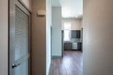 This single-floor unit presents a clean, contemporary design throughout, characterized by neutral tones, light wood-look flooring in common areas, and plush carpet in the bedrooms. The kitchen is a notable highlight, outfitted with a full suite of stainless steel appliances including a side-by-side refrigerator with ice maker, electric range, built-in microwave, and dishwasher. Cabinetry combines high-gloss grey upper cabinets with wood-grain lower cabinets, complemented by a light tile backsplash and ample counter space. A window above the sink provides natural light and exterior views. The bedrooms are generously sized, with one featuring notably tall ceilings and large windows that allow abundant sunlight to fill the room. A walk-in closet outfitted with wire shelving and hanging rods provides substantial storage capacity. Two full bathrooms mirror each other in design, each featuring a soaking tub with shower combination, light stone-look tile flooring, and a wood-toned wall cabinet. The hallway houses a dedicated laundry closet with a stacked washer and dryer unit, adding everyday convenience. Recessed lighting and a smart thermostat round out the modern finishes throughout.