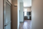 This single-floor unit presents a clean, contemporary design throughout, characterized by neutral tones, light wood-look flooring in common areas, and plush carpet in the bedrooms. The kitchen is a notable highlight, outfitted with a full suite of stainless steel appliances including a side-by-side refrigerator with ice maker, electric range, built-in microwave, and dishwasher. Cabinetry combines high-gloss grey upper cabinets with wood-grain lower cabinets, complemented by a light tile backsplash and ample counter space. A window above the sink provides natural light and exterior views. The bedrooms are generously sized, with one featuring notably tall ceilings and large windows that allow abundant sunlight to fill the room. A walk-in closet outfitted with wire shelving and hanging rods provides substantial storage capacity. Two full bathrooms mirror each other in design, each featuring a soaking tub with shower combination, light stone-look tile flooring, and a wood-toned wall cabinet. The hallway houses a dedicated laundry closet with a stacked washer and dryer unit, adding everyday convenience. Recessed lighting and a smart thermostat round out the modern finishes throughout.