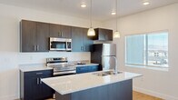 This thoughtfully laid-out 1-bedroom, 1-bathroom unit combines modern design with functional living across a single floor. The kitchen serves as the heart of the space, featuring a large central island with a granite-look countertop, double undermount sink, and pendant lighting overhead. Dark espresso cabinetry extends to the ceiling, providing ample storage, while stainless steel appliances — including a refrigerator, range, microwave, and dishwasher — complete the contemporary look. Light hardwood-style flooring flows throughout the main living areas, enhancing the bright, open atmosphere. The living area benefits from a sliding glass door that invites natural light and provides access to an outdoor space. The bedroom is a comfortable retreat, finished with plush carpet and dual windows that frame outdoor views and fill the room with natural light. A generously sized walk-in closet with dual hanging rods offers excellent storage capacity. The bathroom features a dark navy vanity with granite-look countertops, a large mirror, and warm wood-tone flooring, creating a clean and modern aesthetic. Throughout the unit, white walls and recessed lighting contribute to a fresh, contemporary ambiance.