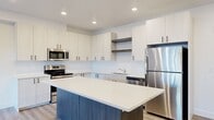 This well-appointed 3-bedroom, 1-bathroom residence offers a thoughtfully designed single-floor layout with a clean, modern aesthetic. The open-concept kitchen and living area serves as the heart of the home, where the kitchen stands out with crisp white upper cabinetry, dark lower cabinets, and a striking center island with a white quartz countertop and contrasting wood-toned base. Stainless steel appliances — including a refrigerator, range, microwave, and dishwasher — complete the space. Light wood-style luxury vinyl flooring flows throughout the main living areas, complemented by recessed lighting and bright white walls that create an airy, inviting atmosphere. The living room extends naturally from the kitchen and features a sliding glass door dressed with vertical blinds, allowing ample natural light and outdoor access. The primary bedroom offers hardwood-style flooring and generous wall space, while the two additional bedrooms feature plush carpeting and ample closet storage, including double closets in one room. The bathroom is finished with a full-width vanity mirror, an undermount sink set in a white countertop, and clean, minimalist fixtures. Throughout the residence, recessed lighting, crisp white walls, and consistent finishes create a cohesive and modern living environment.