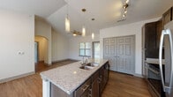 This single-story unit is designed with an open-concept layout that seamlessly connects the kitchen, dining, and living areas. The kitchen serves as the centerpiece, anchored by a large island with a double stainless steel sink and granite countertops. Dark espresso cabinetry provides ample storage, while a white subway tile backsplash adds contrast. Stainless steel appliances, including a refrigerator, electric range, and over-the-range microwave, complete the well-equipped cooking space. Pendant lighting hangs above the island, complementing track lighting overhead.

The living area features soaring vaulted ceilings and hardwood-style flooring, creating an airy, open feel enhanced by natural light from multiple windows. A ceiling fan adds to the comfort of the space. An arched doorway adds an architectural detail connecting adjacent areas.

The bedrooms are carpeted and include ceiling fans and windows that bring in natural light. The bathrooms are finished with granite-topped dark vanities and tile flooring. One bathroom features a walk-in shower, while another offers a more compact layout. A large double-door closet provides generous storage within the living space.