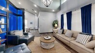 Located at 1000 Archive Cir in Oxford, Mississippi, this single-floor amenity space delivers a contemporary and functional environment designed for both relaxation and productivity. The open layout is anchored by a stylish lounge area with vaulted ceilings, an elegant chandelier, and rich wood-look flooring throughout. A plush seating arrangement featuring neutral and blue leather sofas surrounds a round wooden coffee table, creating an inviting gathering space accented by bold navy curtains and natural light from large windows.

A dramatic centerpiece — a towering illuminated structure with vivid blue backlit panels — divides the lounge from a casual dining and work area, adding a striking architectural focal point. The adjacent area features a long wooden communal table with bench seating, complemented by a colorful large-format art piece on the wall and direct access to the outdoors through glass double doors.

Two glass-enclosed private meeting rooms, furnished with ergonomic chairs and wall-mounted displays, offer dedicated spaces for focused work or small group collaboration. A built-in workstation with computer access rounds out the business center amenities. Throughout, the space maintains a cohesive palette of cool grays, blues, and warm wood tones, achieving a balance of modern design and everyday functionality.