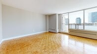 Located at 100 Parkway Forest Dr in Toronto's Parkway Forest neighbourhood, this well-appointed 2-bedroom, 1-bathroom unit offers a functional and comfortable layout across a single floor. Classic parquet flooring runs throughout the main living areas and bedrooms, lending warmth and a timeless character to the space.

The open living room is bright and airy, benefiting from floor-to-ceiling windows that frame views of the surrounding Toronto cityscape. A sliding door leads to a private balcony, extending the living space outdoors. The kitchen is thoughtfully designed with white shaker-style cabinetry, stainless steel appliances including a refrigerator, range, and dishwasher, a subway tile backsplash, and light large-format tile flooring. A peninsula counter provides additional workspace and separates the kitchen from the adjacent living area.

Both bedrooms are well-proportioned, featuring the same warm parquet flooring, neutral walls, and double-door closets offering ample storage. The primary bedroom is generously sized. The bathroom is clean and bright, finished with classic white subway tile surrounding a full soaking tub and shower combination. A central hallway connects all rooms in an efficient and logical flow, making the overall layout practical for everyday living.