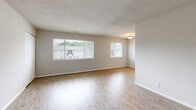 Located at 1716 Pennwood Dr in Hampton, Virginia, this single-floor residence offers a clean, functional layout with a neutral color palette throughout. The spacious living area is a standout feature, showcasing light-toned hardwood-style flooring that reflects natural light streaming in through multiple large windows fitted with blinds. A textured ceiling adds subtle character, while the open feel of the space lends itself to versatile furniture arrangements. An additional area near the entryway also features the same hardwood-style flooring, a closet for storage, and window access to natural light. The kitchen is well-equipped, featuring rich dark wood cabinetry, light granite-style countertops, and a black gas range with an overhead exhaust hood, offering both style and practicality for cooking. The bedrooms are carpeted in a warm tan tone, providing comfort underfoot. Each bedroom includes windows that allow natural light in, and at least one bedroom features a wide reach-in closet with a full-width hanging rod, offering generous storage. The bathroom includes a tiled tub-shower combination with classic white square tiles and a dark border accent, a wood-toned vanity with under-sink storage, a toilet, and tile flooring. Overall, the home presents a tidy, move-in ready environment with consistent finishes throughout.