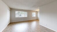 Located at 1716 Pennwood Dr in Hampton, Virginia, this single-floor residence offers a clean, functional layout with a neutral color palette throughout. The spacious living area is a standout feature, showcasing light-toned hardwood-style flooring that reflects natural light streaming in through multiple large windows fitted with blinds. A textured ceiling adds subtle character, while the open feel of the space lends itself to versatile furniture arrangements. An additional area near the entryway also features the same hardwood-style flooring, a closet for storage, and window access to natural light. The kitchen is well-equipped, featuring rich dark wood cabinetry, light granite-style countertops, and a black gas range with an overhead exhaust hood, offering both style and practicality for cooking. The bedrooms are carpeted in a warm tan tone, providing comfort underfoot. Each bedroom includes windows that allow natural light in, and at least one bedroom features a wide reach-in closet with a full-width hanging rod, offering generous storage. The bathroom includes a tiled tub-shower combination with classic white square tiles and a dark border accent, a wood-toned vanity with under-sink storage, a toilet, and tile flooring. Overall, the home presents a tidy, move-in ready environment with consistent finishes throughout.