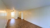This single-floor residence offers a straightforward and functional layout designed for comfortable everyday living. The main living area is defined by rich, dark hardwood-style flooring that extends throughout, providing a warm and cohesive look underfoot. Neutral, light-toned walls create a bright and airy atmosphere, while the textured popcorn ceiling adds a classic architectural detail overhead. A ceiling fan is centrally positioned in the living space, promoting year-round air circulation and comfort. Natural light filters in through a window visible toward the rear of the space, enhancing the open feel of the interior. Multiple doorways lead to additional rooms, suggesting a practical floor plan with clear separation between living and private areas. White interior doors and clean baseboards contribute to the tidy, understated aesthetic throughout. The overall ambiance is calm and neutral, offering a blank canvas well-suited for personalization. The space presents a simple yet livable environment that balances functionality with an unpretentious residential character.