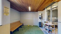 Located at 360 W 200 S in downtown Salt Lake City, this thoughtfully designed pet amenity space offers a complete environment for residents and their four-legged companions. The facility is organized into two distinct functional areas, each serving a specific purpose for pet care and recreation.

The main play area is finished with a striking warm-toned wood plank ceiling that lends a refined, welcoming character to the space. Artificial turf flooring covers a generous portion of the room, providing a comfortable and hygienic surface for pets to play. A wooden bench along the wall offers seating for pet owners, while a waste bag dispenser and waste bin ensure easy cleanup. Toys and treats are neatly organized on open shelving near the entrance, and a large window allows natural light to filter in, offering views of the surrounding urban streetscape.

Adjacent to the play area is a dedicated grooming station, separated by full-height glass partitions and aluminum-framed doors that maintain visual connectivity between the zones. This area features a deep stainless steel wash tub equipped with a spray hose, set against a tiled wall backdrop, and is complemented by tile flooring for easy maintenance. Framed pet-themed artwork adorns the walls, adding a charming finishing touch. Together, the two areas form a cohesive, well-appointed pet amenity suite.